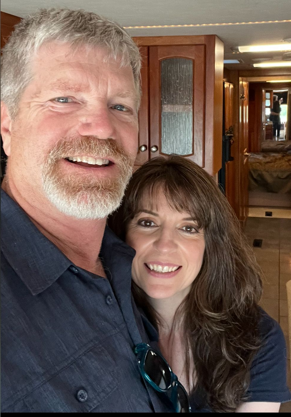 Smiling couple posing indoors in a wood-paneled hallway, with a doorway and mirror behind them.
