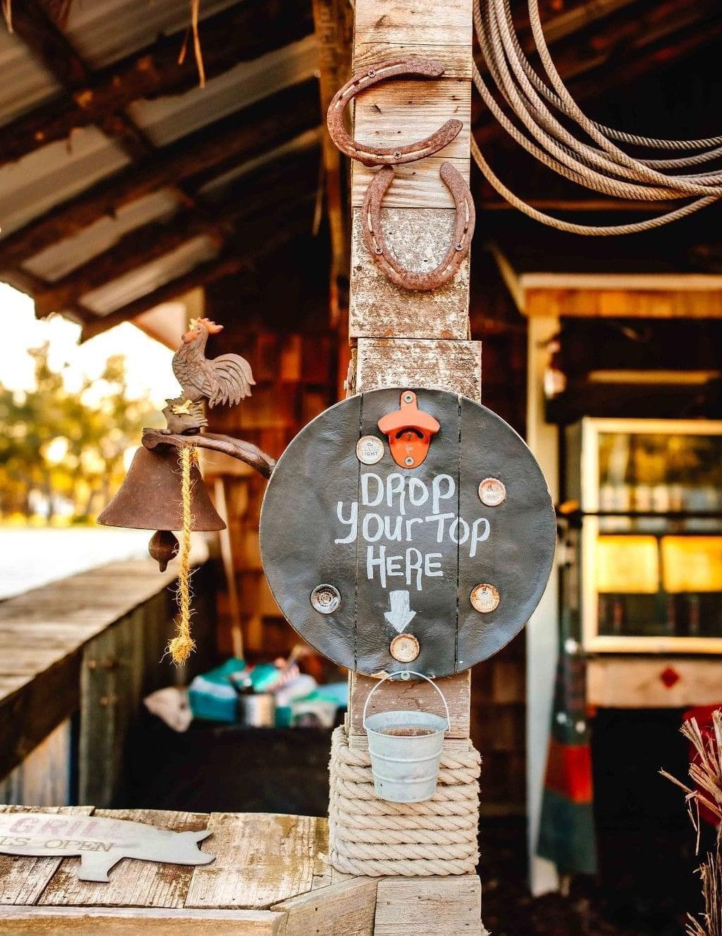 Rustic sign reading “Drop your top here” on a weathered post outside a beach shack.