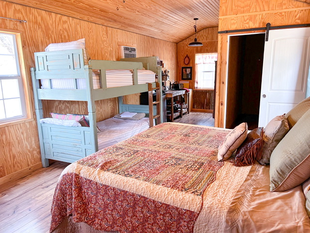Rustic bedroom with blue bunk bed, wood walls, and a tan bed in the foreground