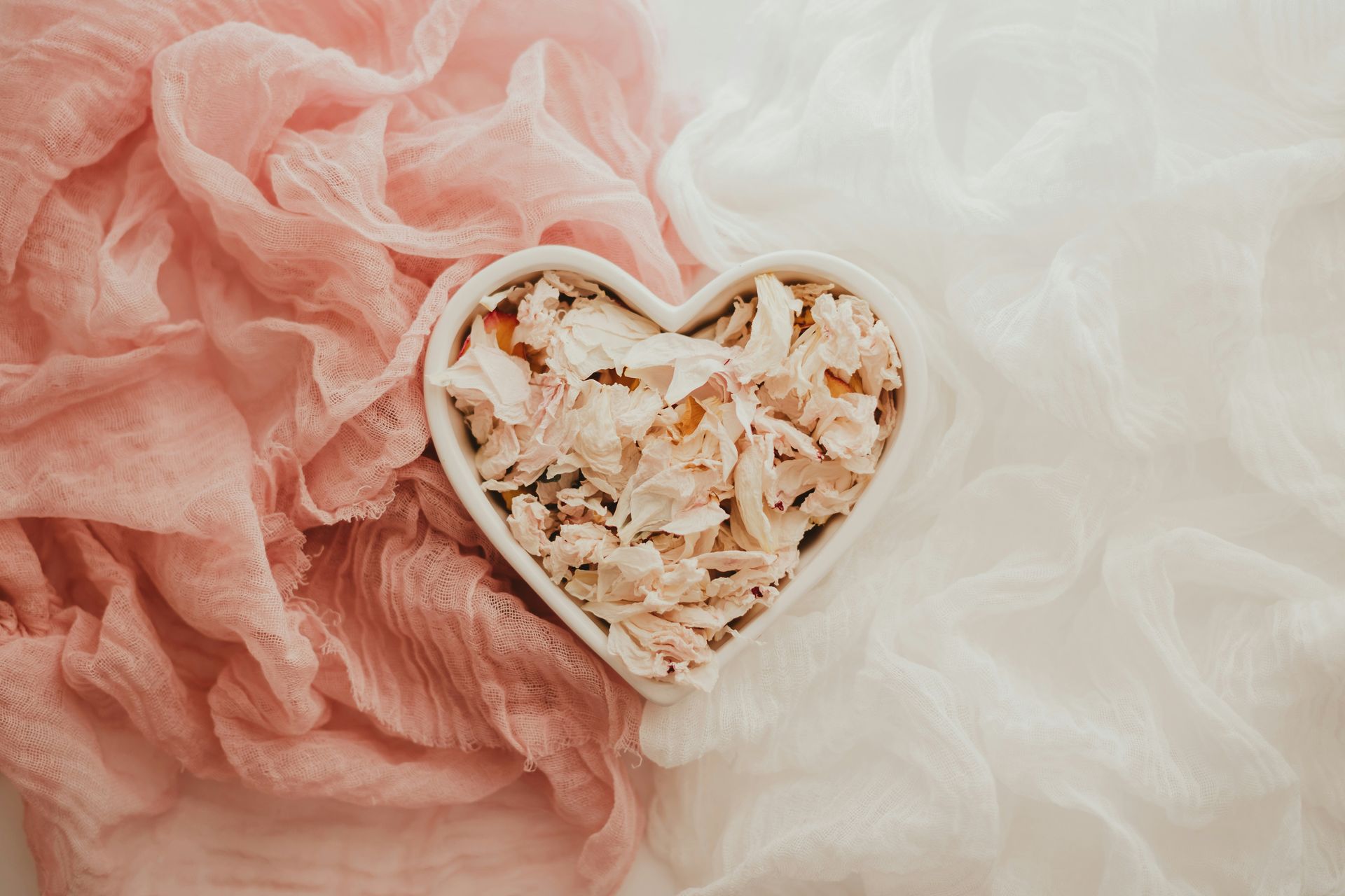 Heart-shaped bowl of pink and white potpourri on soft pink and cream fabric