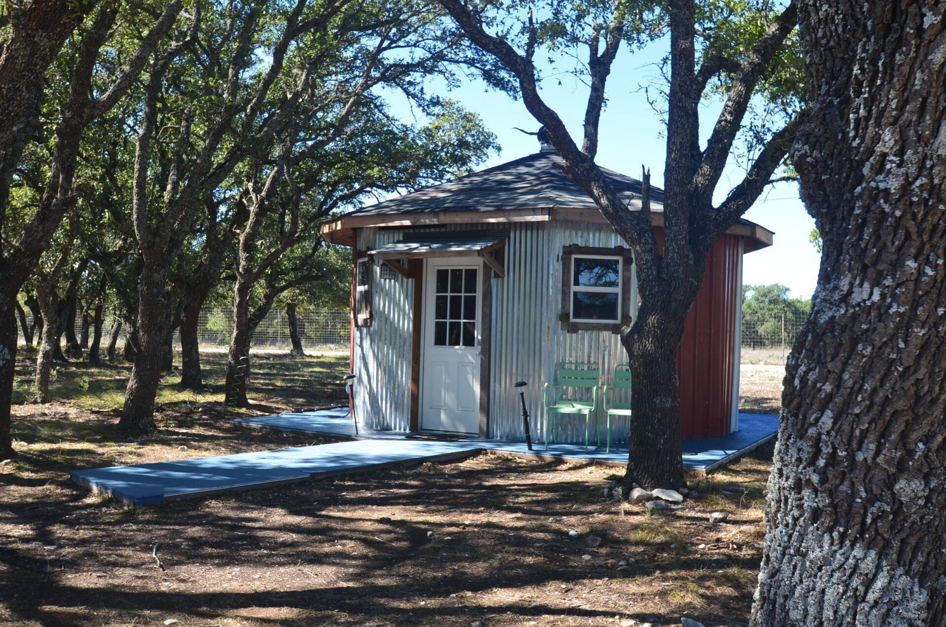 Small white shed in a wooded area, with trees and dry ground around it