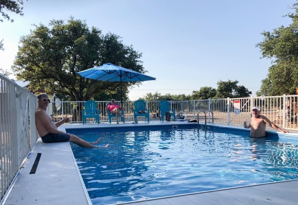Two people relaxing by a blue outdoor pool under a blue umbrella on a sunny day