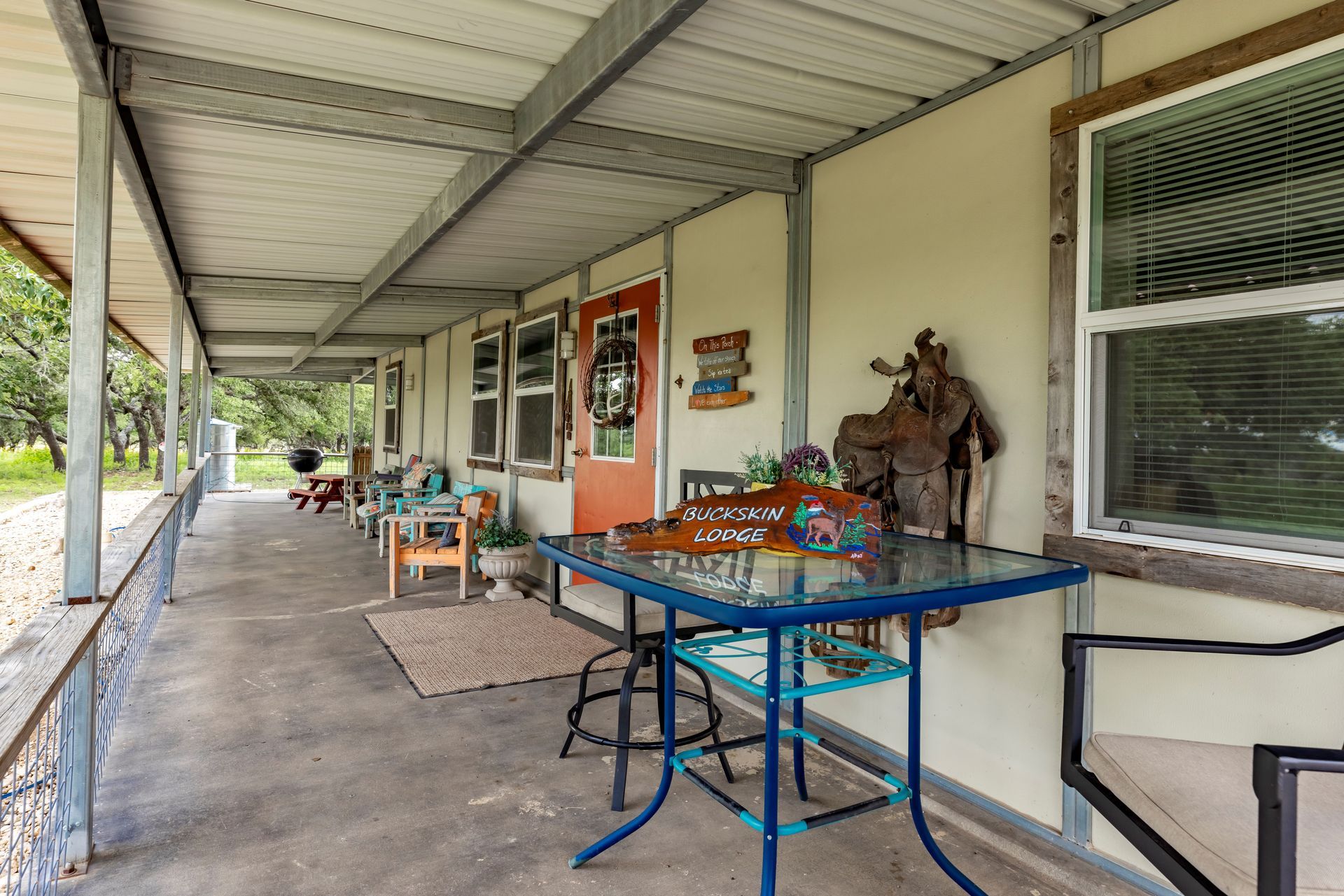 Covered porch with tables, chairs, and potted decor along a beige house wall