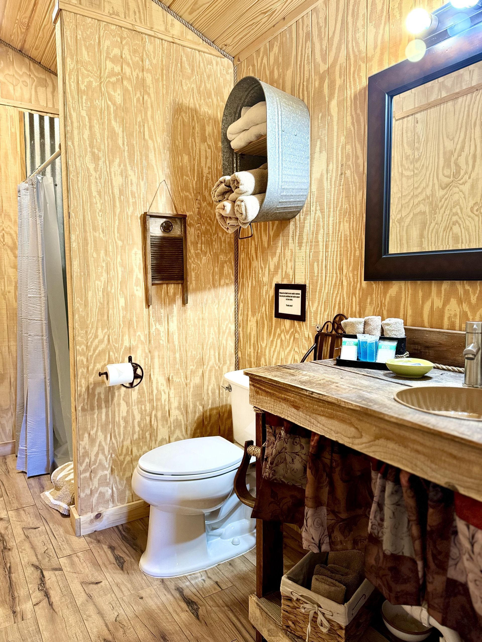 Small rustic bathroom with toilet, sink, mirror, and woven wall decor above the toilet