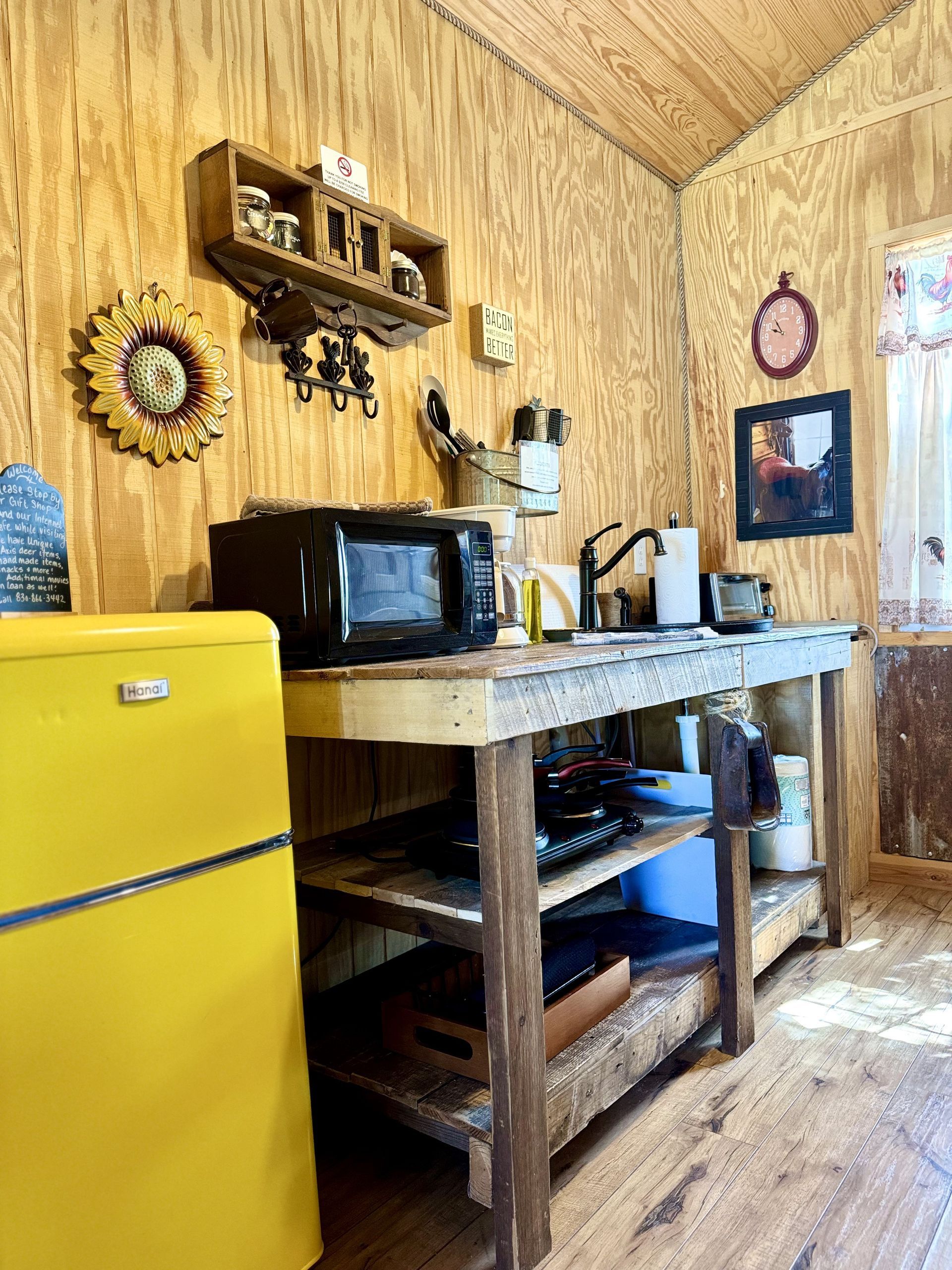 Rustic kitchen with yellow fridge, wood counter, microwave, and shelves in a cozy wood-paneled room