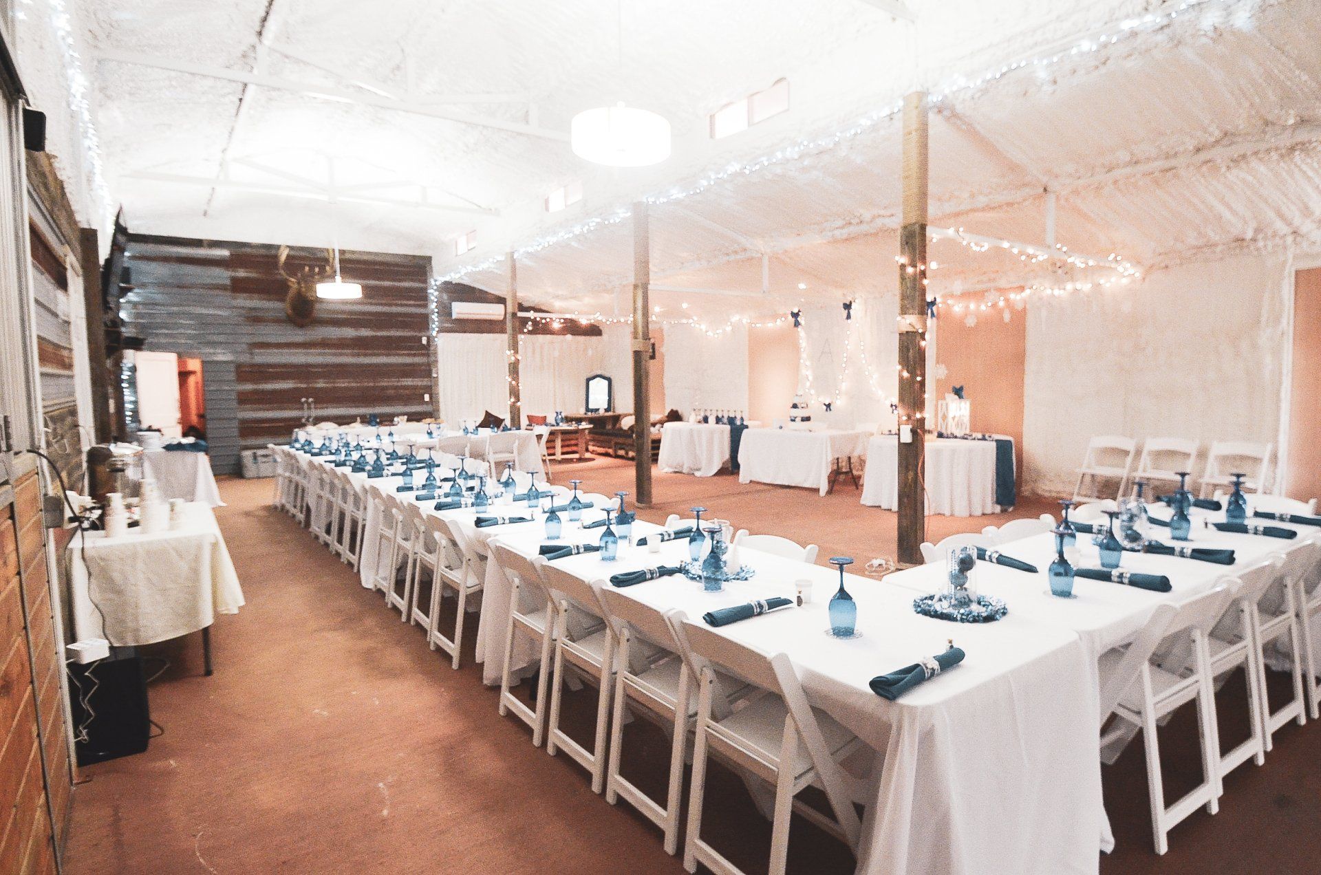 Long banquet table set with white linens and blue napkins in a bright tented event space