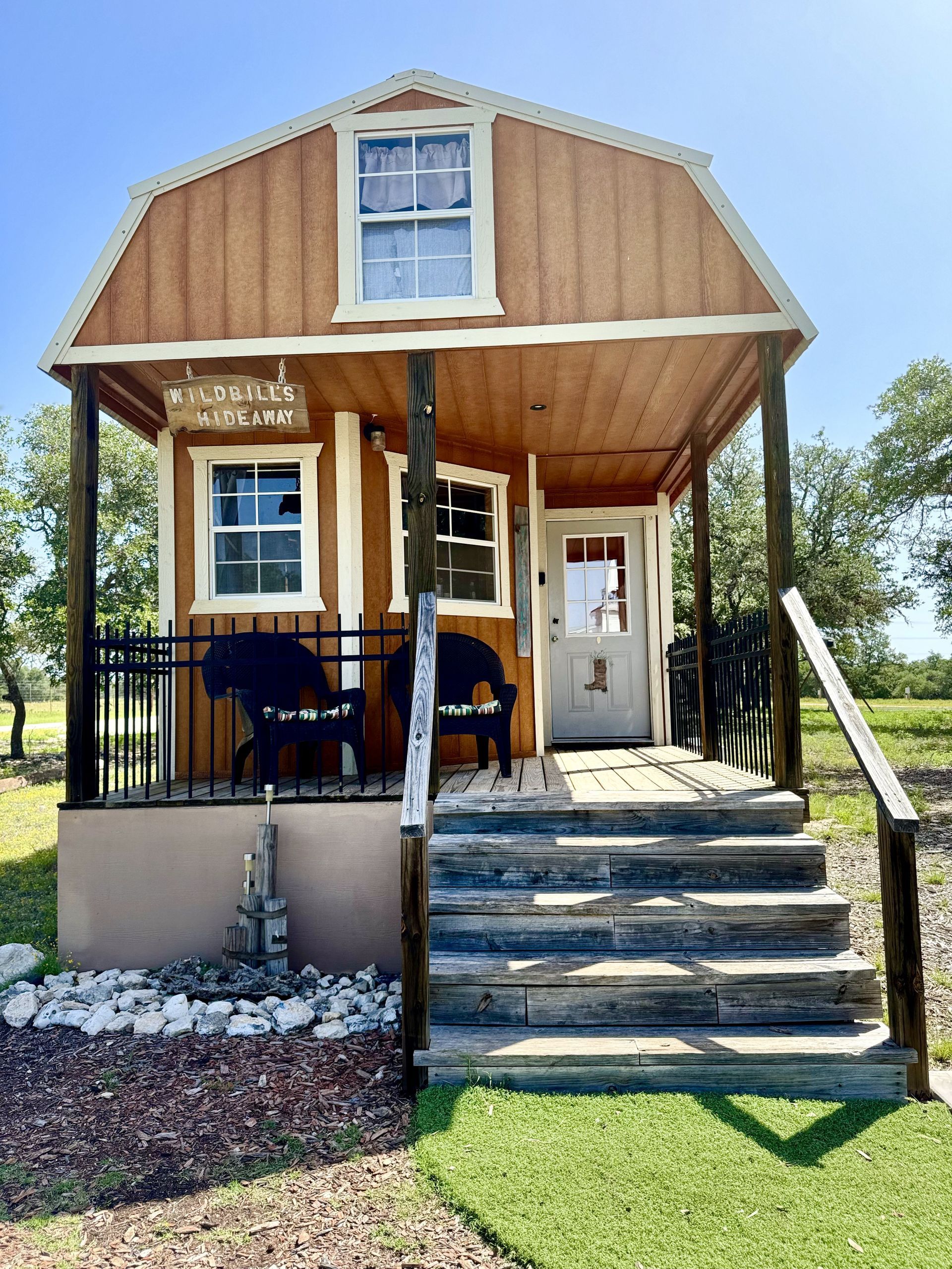 Small wooden cabin with front porch, steps, and white-trimmed windows on a grassy lot