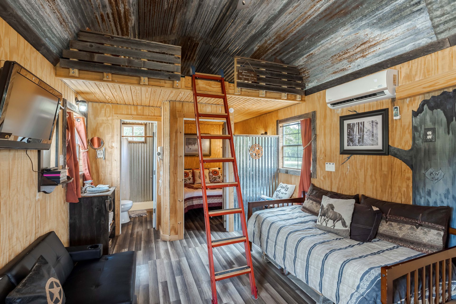 Tiny rustic bedroom with loft ladder, bed, couch, and wood-paneled walls