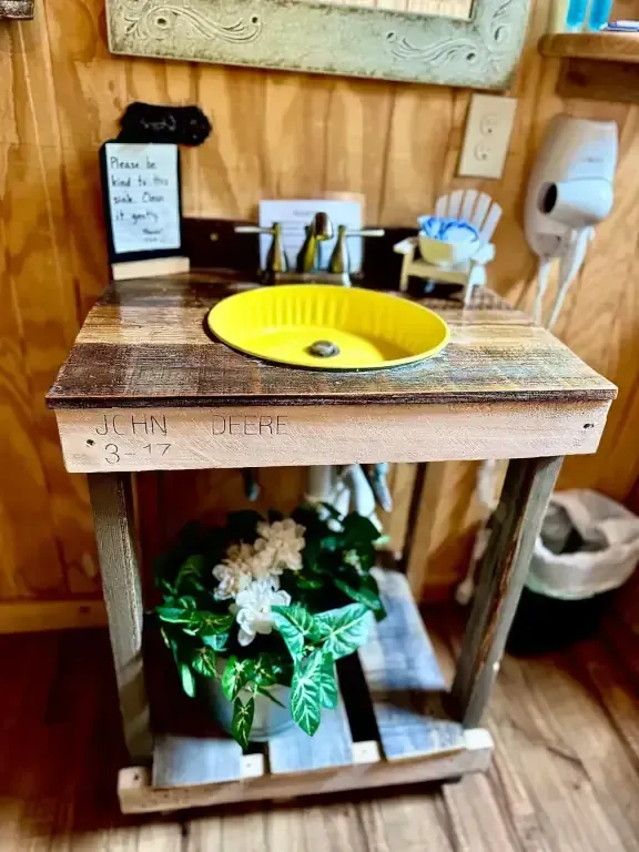 Miniature bathroom sink display with yellow basin, faucet, and tiny shelf items under a wooden counter