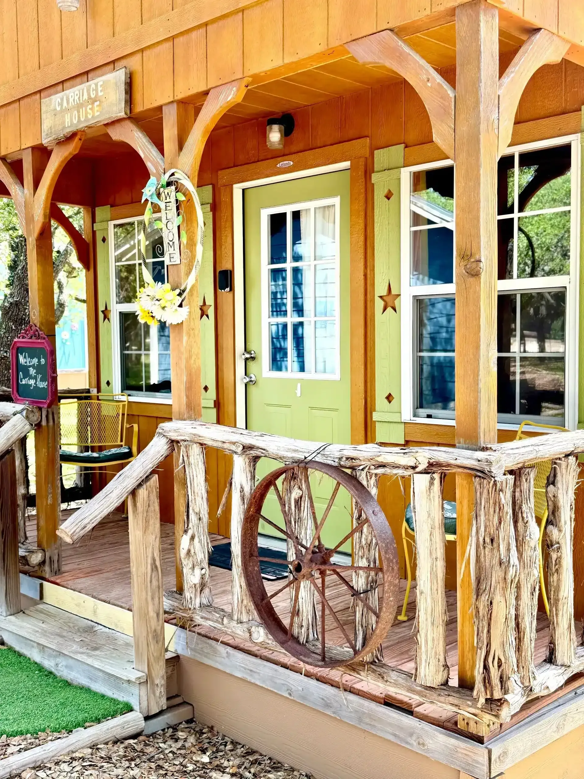 Rustic wooden porch with wagon wheel railing, green door, and hanging wheel decoration.