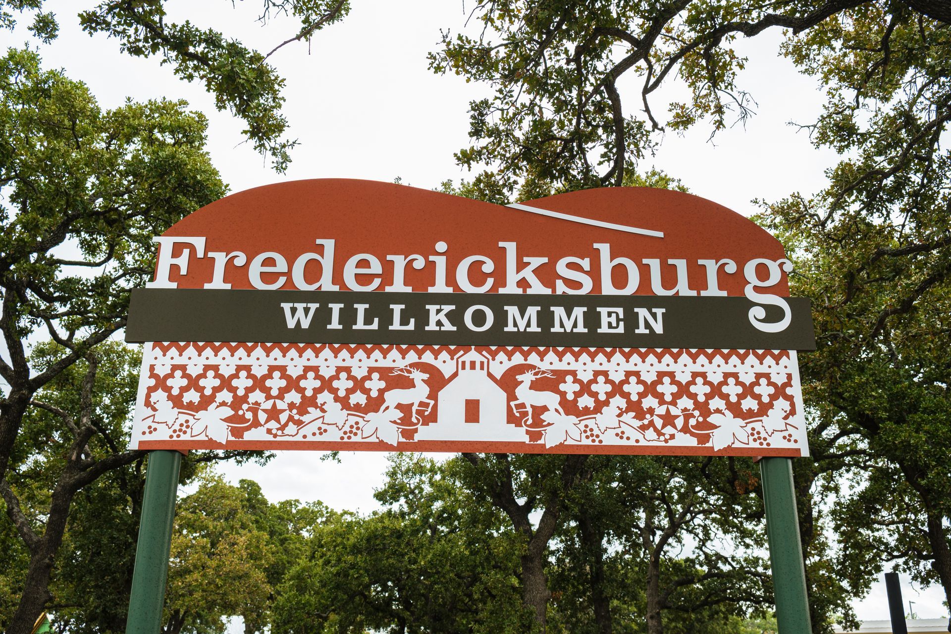 Fredericksburg welcome sign with red lettering and white floral trim among trees