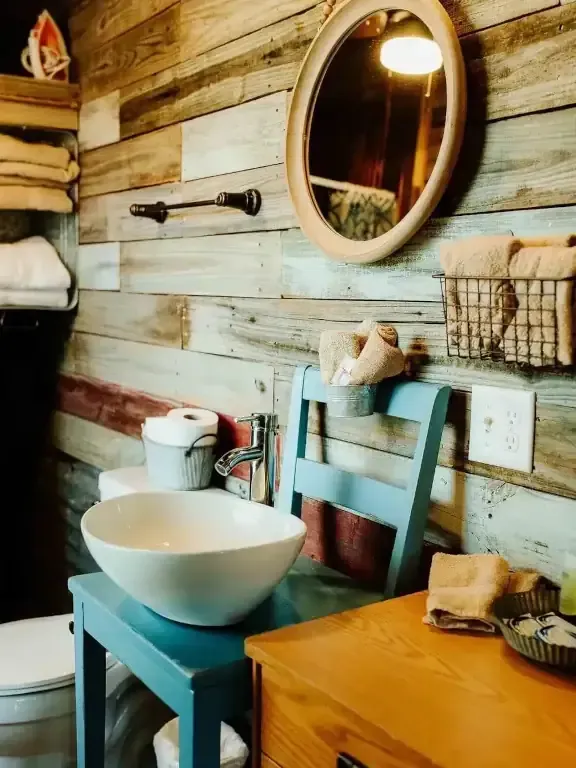 Rustic bathroom vanity with turquoise sink stand, oval mirror, wood plank wall, and woven storage basket