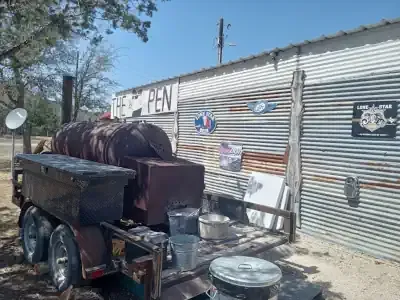 Outdoor yard with a trailer, metal pots, and tools beside a corrugated metal shed.