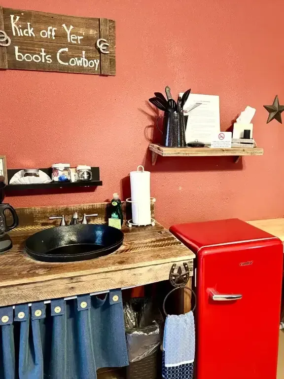 Rustic bathroom sink area with red fridge, wooden counter, black basin, and cowboy sign on coral wall