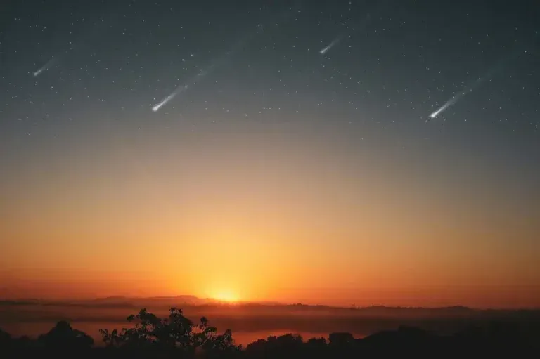 Sunset over a dark horizon with glowing orange sky and a bright comet-like streak above