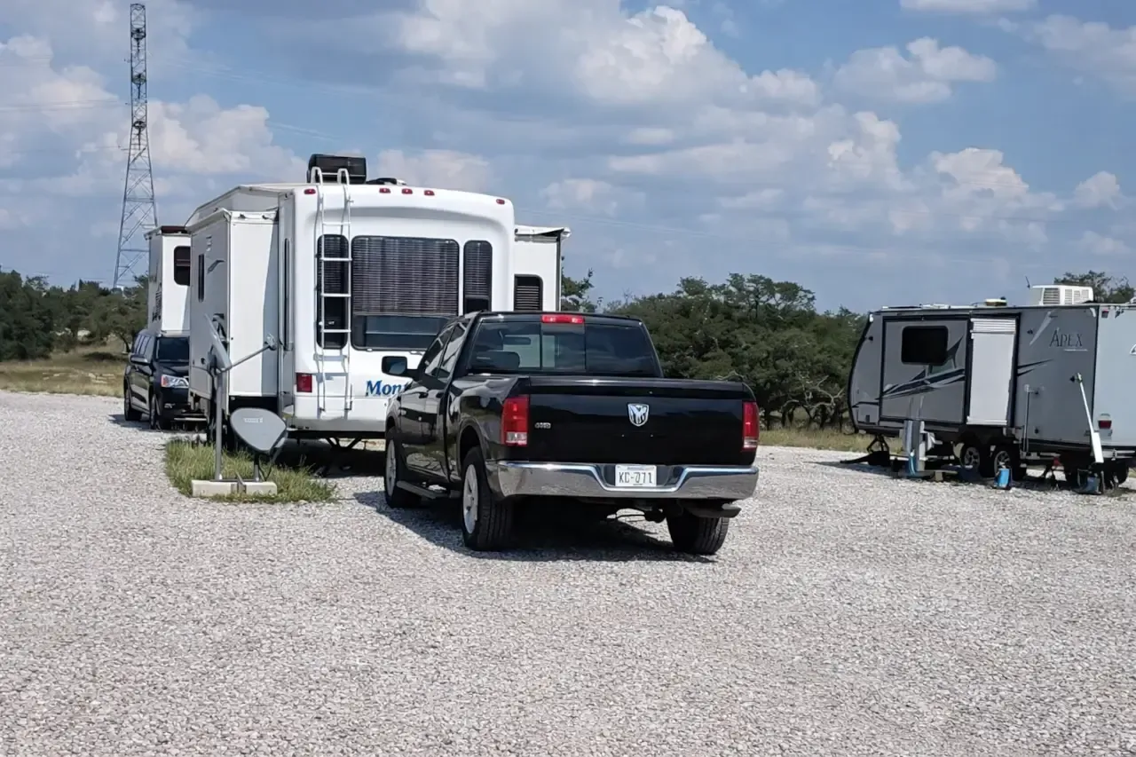 Black pickup parked beside a white RV and trailer on a gravel lot under a cloudy sky