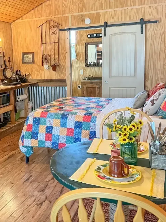 Cozy bedroom with patchwork quilt, barn door, sunflower tray table, and wood-paneled walls