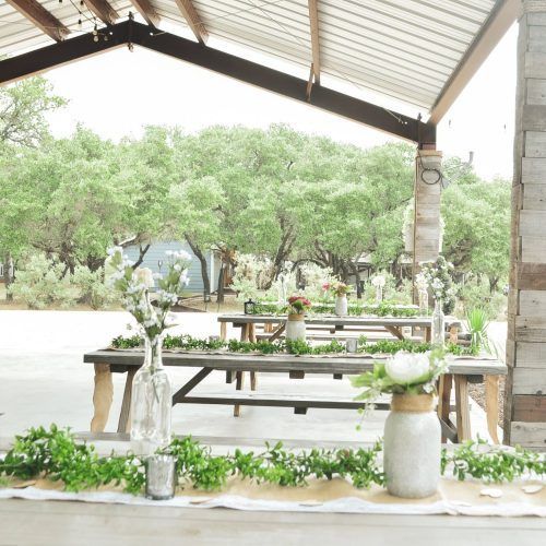 Outdoor rustic pavilion with wooden picnic tables, white floral decor, and trees in the background