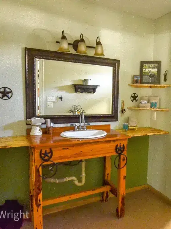 Bathroom vanity with large mirror, wall sconces, wooden sink cabinet, and green accent wall.