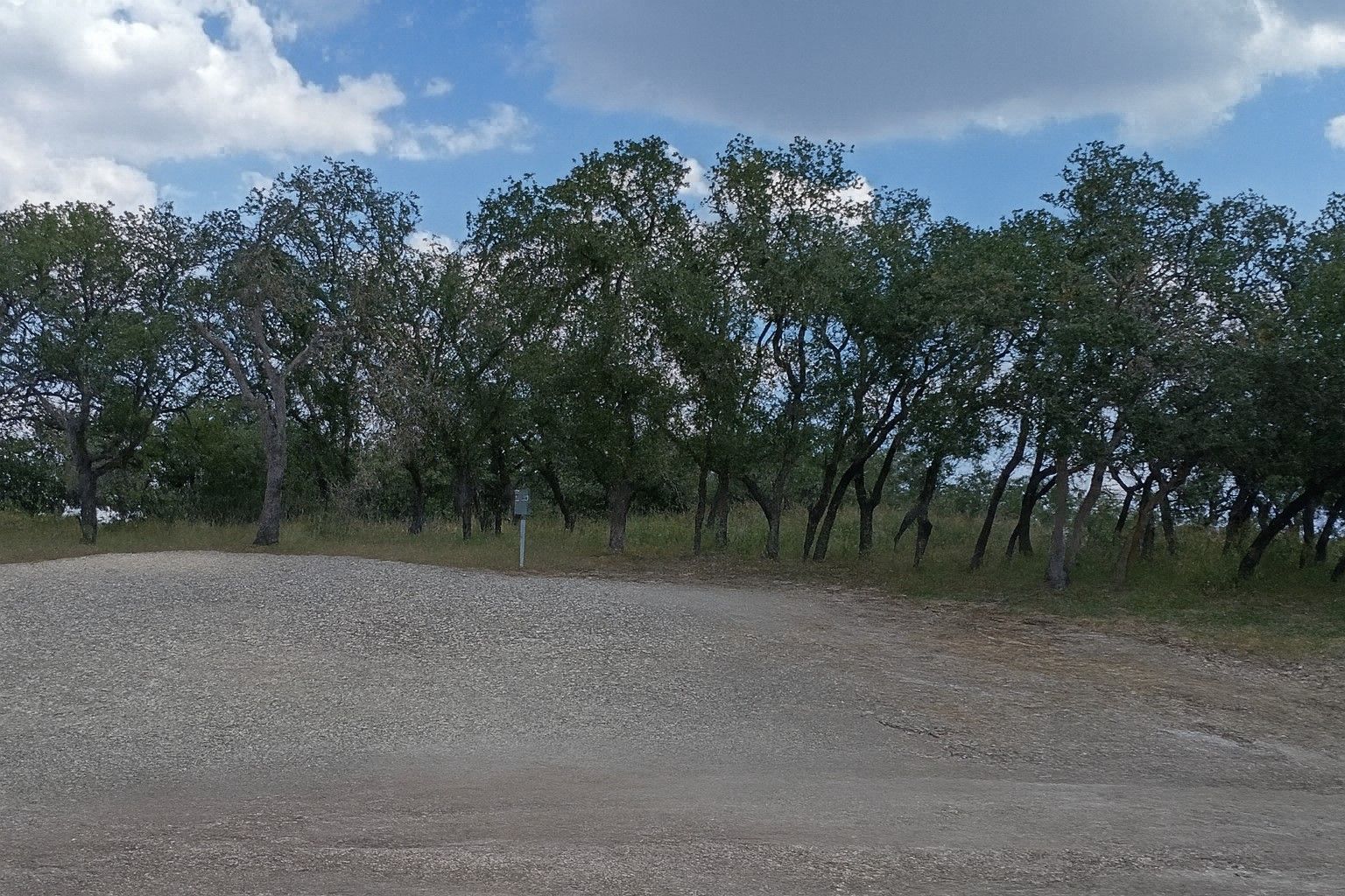 Gravel clearing with scattered green trees under a partly cloudy blue sky
