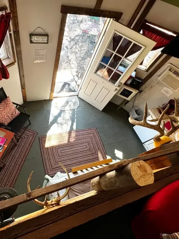 Small shop interior with open front door, sunlight on floor, and shelves by the entrance