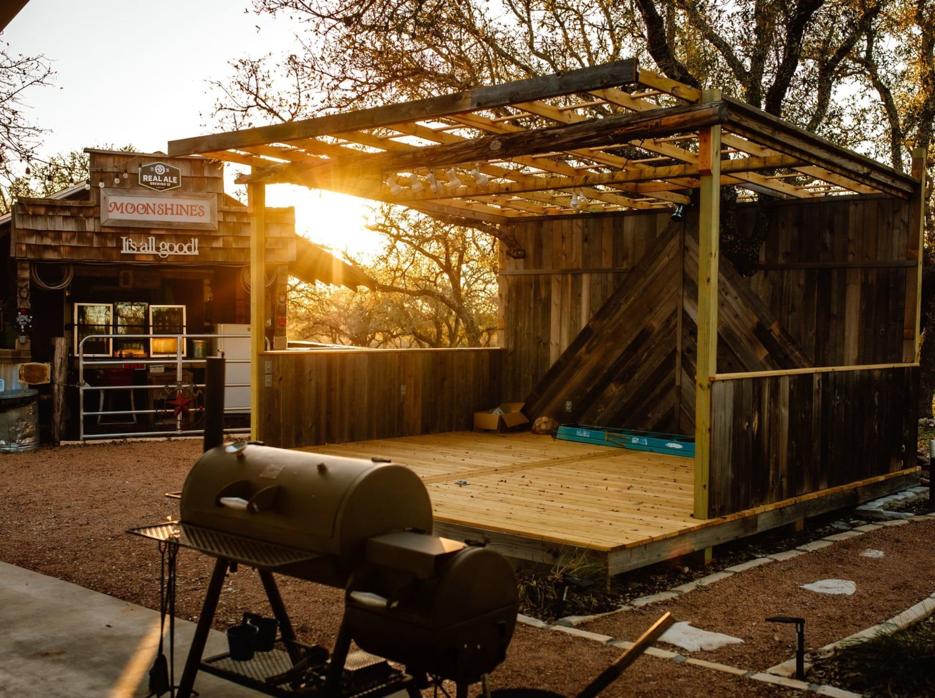 Sunlit outdoor wooden stage with pergola and grill in a rustic yard