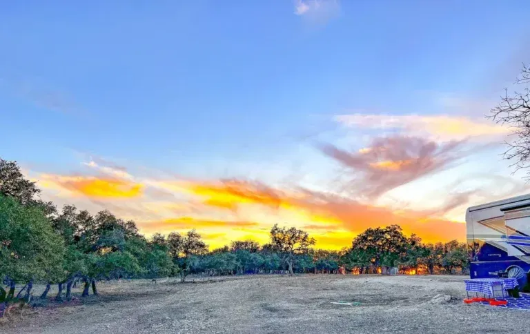 Colorful sunset over a grassy field with trees and a building on the right