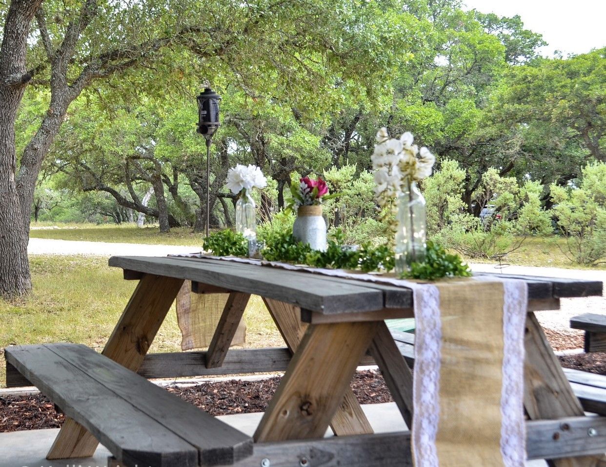 Picnic table decorated with white flowers and a pink bouquet in a park under trees