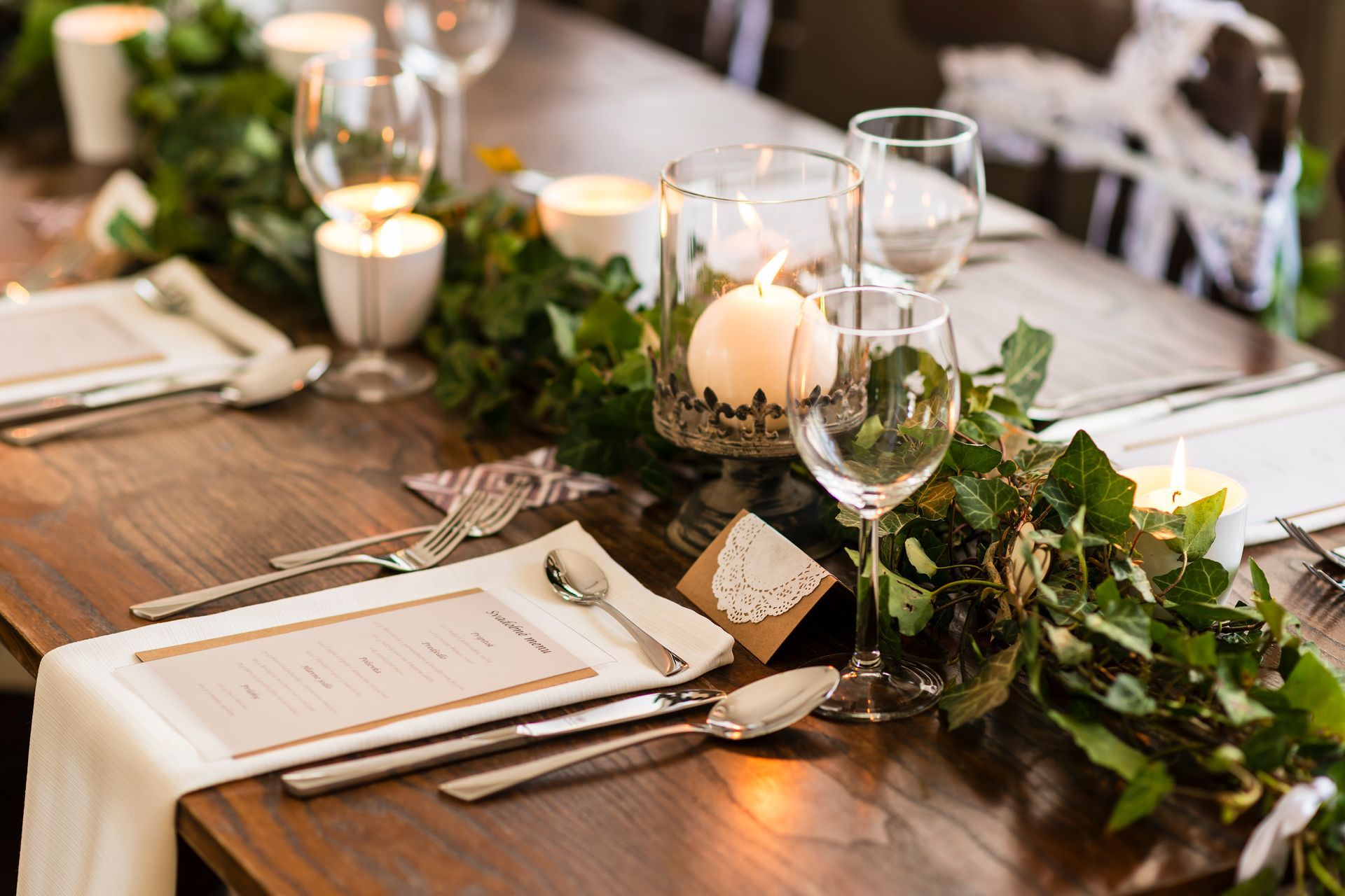 Rustic dining table set with candles, greenery, white napkins, plates, and wine glasses