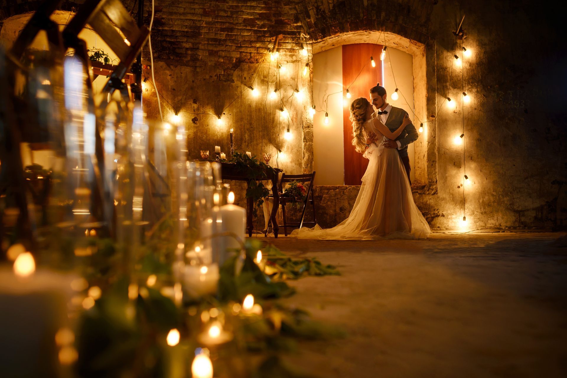 Bride and groom embracing in a warmly lit courtyard with string lights and candles