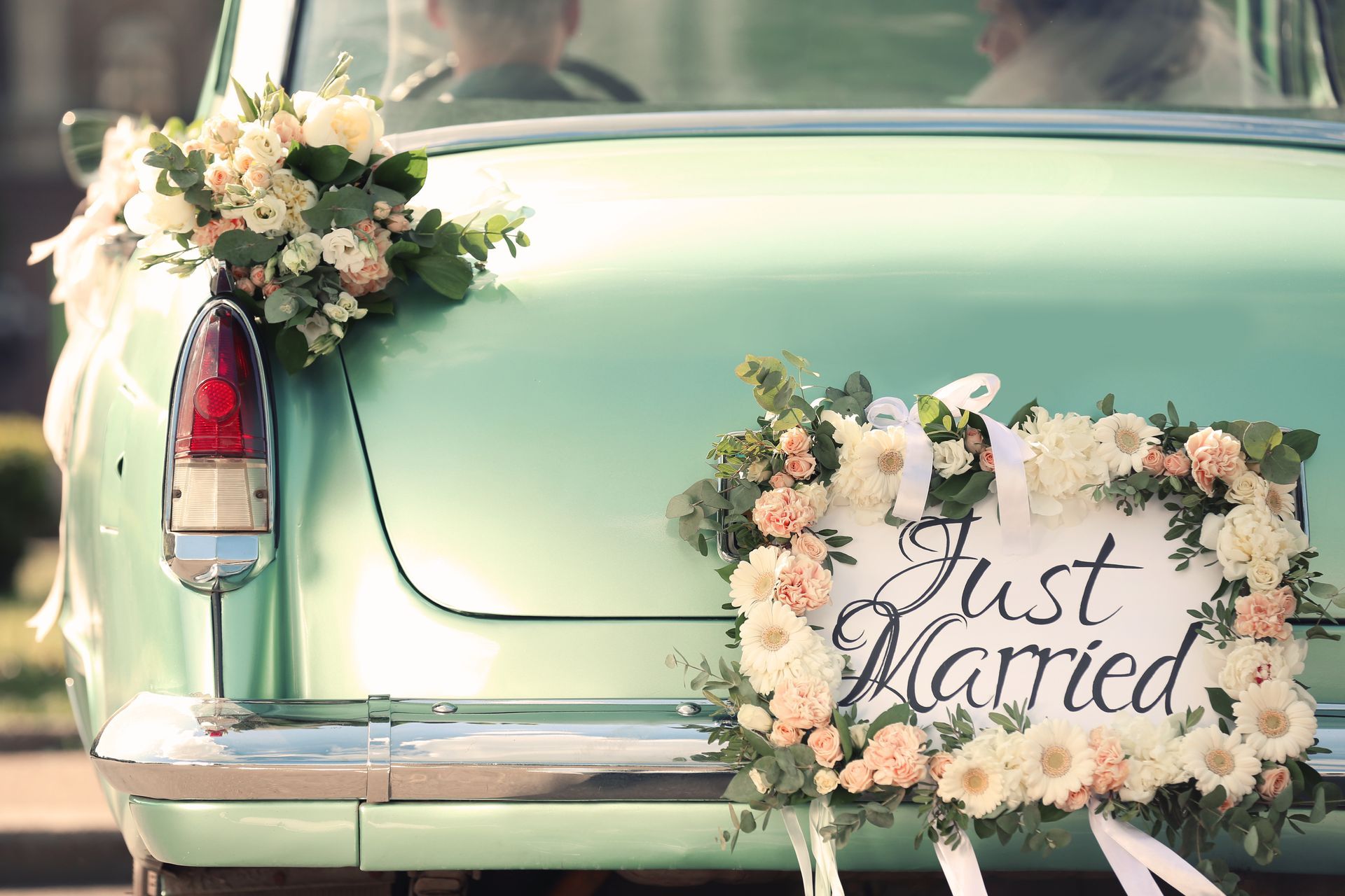 Pastel green car decorated with flowers and a “Just Married” sign on the back.