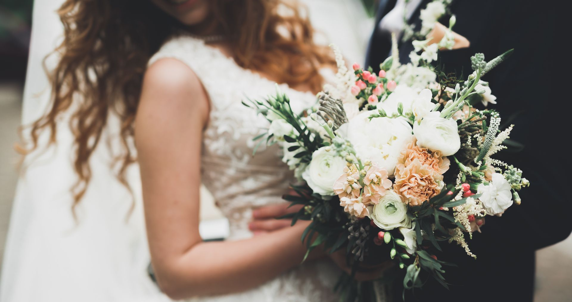 Bride holding a bouquet of white and peach flowers beside a groom in a suit