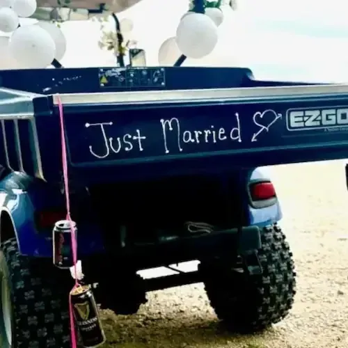 Golf cart decorated for a wedding with “Just Married” sign and balloons, parked on a beach