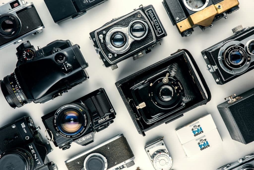 Assorted digital cameras and lenses arranged on a light background in a flat lay.