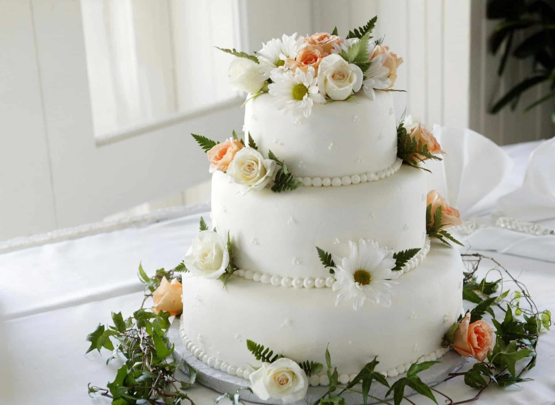 Three-tier white wedding cake with white and peach flowers and greenery accents