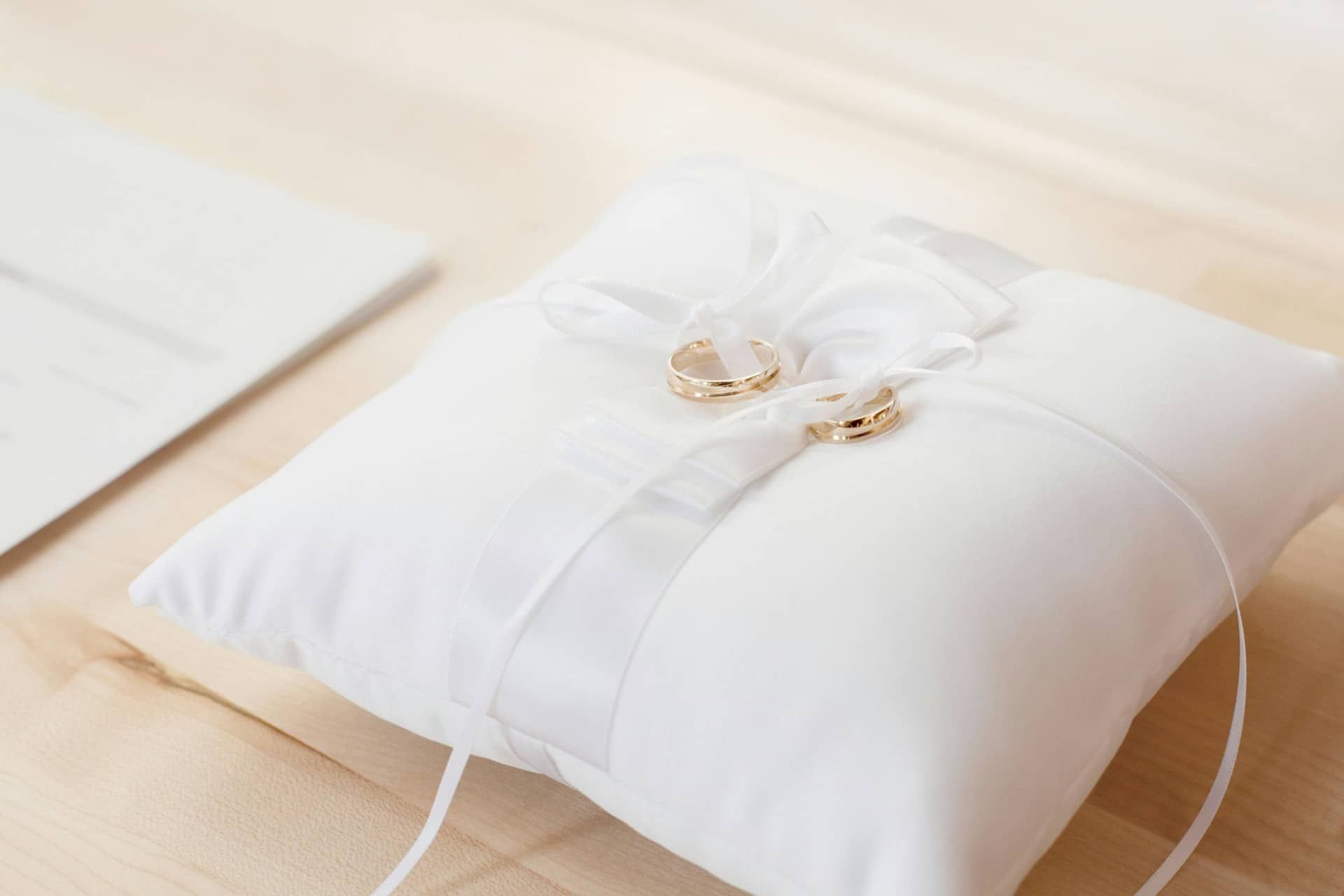 White ring pillow with gold wedding rings on a light wooden table
