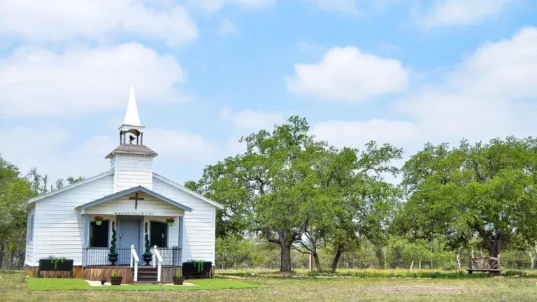Small white church with steeple in a green rural landscape under a blue sky