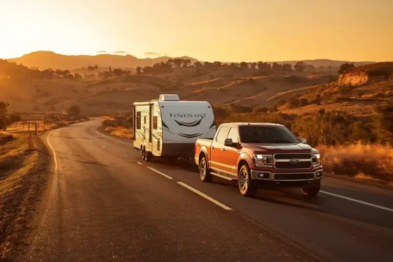 Red pickup truck towing a camper on a winding desert road at sunset