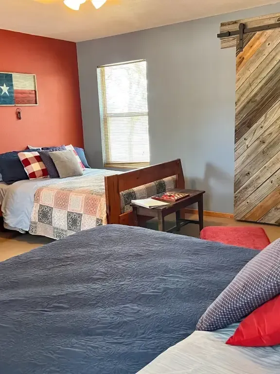 Cozy bedroom with two beds, red accent wall, gray walls, and a window with blinds