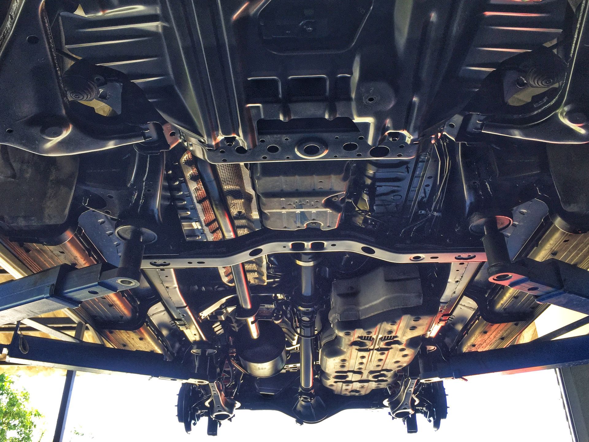 Undercarriage of a car on a lift, showing the chassis, exhaust, and suspension components.