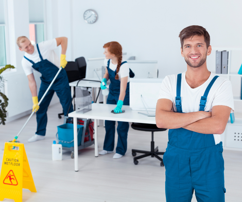 Office cleaning crew mopping a bright workspace, with one cleaner smiling in the foreground.