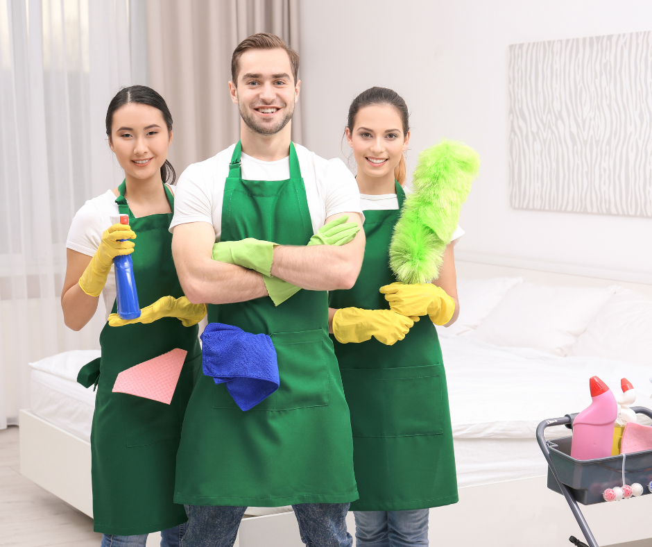 Three cleaners in green aprons with colorful cleaning tools standing in a bright bathroom