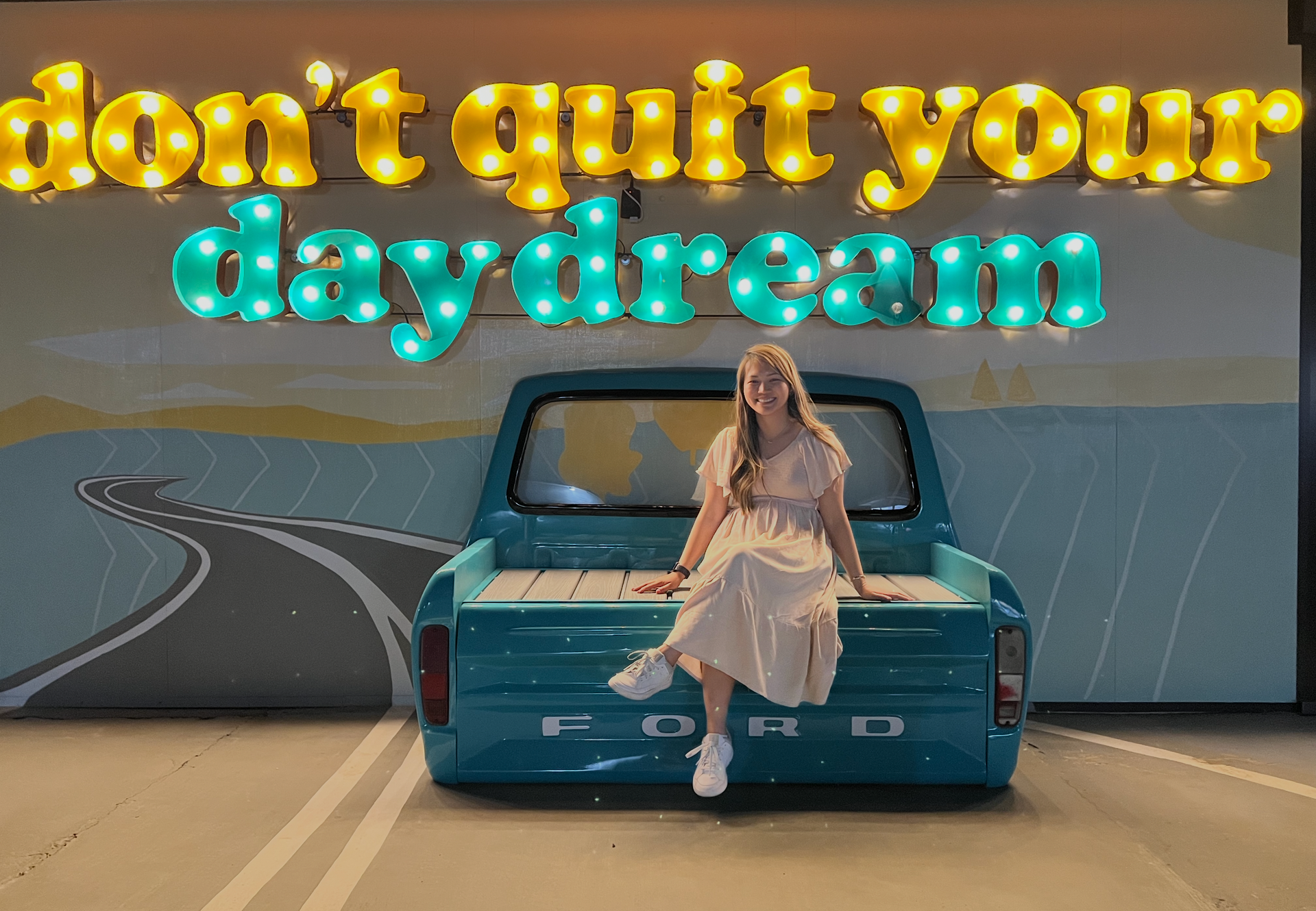 Woman sitting on a teal truck before a mural reading “don’t quit your daydream”
