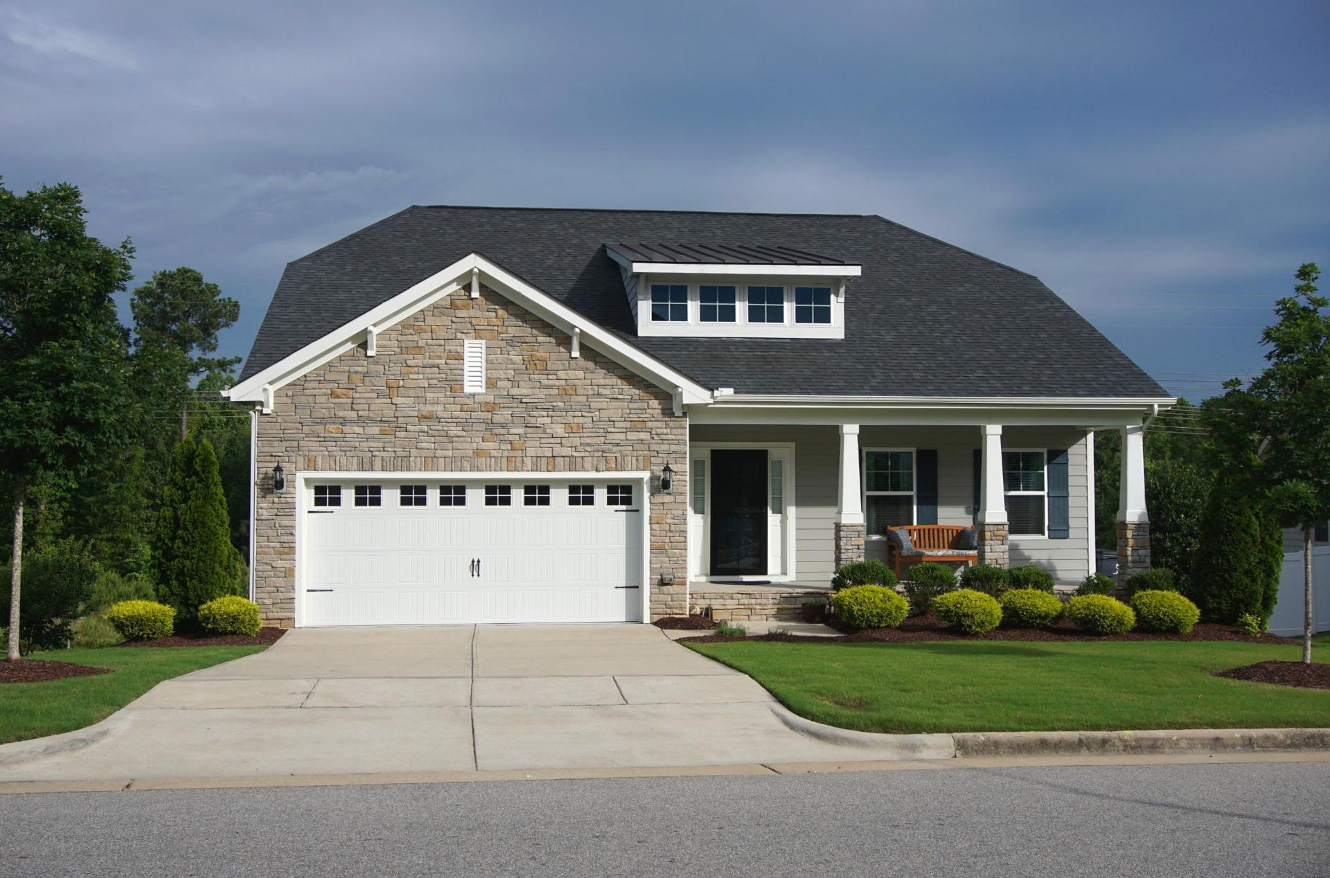 Suburban house with stone facade, white garage, and front porch under a cloudy sky
