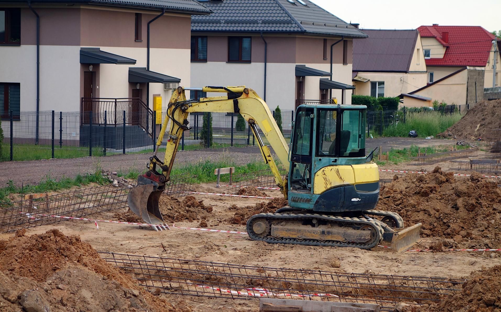 Yellow excavator digging mud at a residential construction site with houses in the background