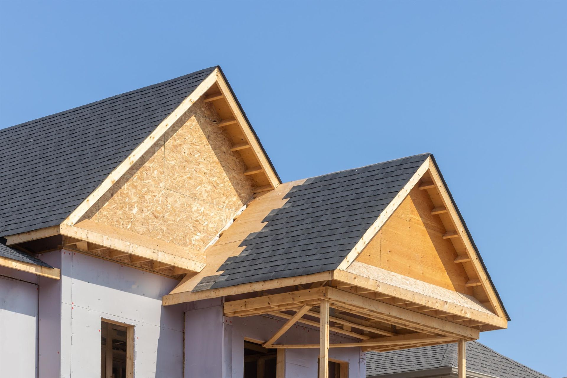Two house rooftops under construction with exposed wood framing against a clear blue sky