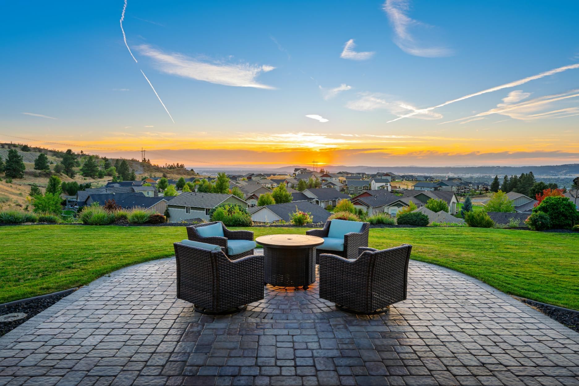 Patio seating overlooking a sunset over a grassy neighborhood and distant hills