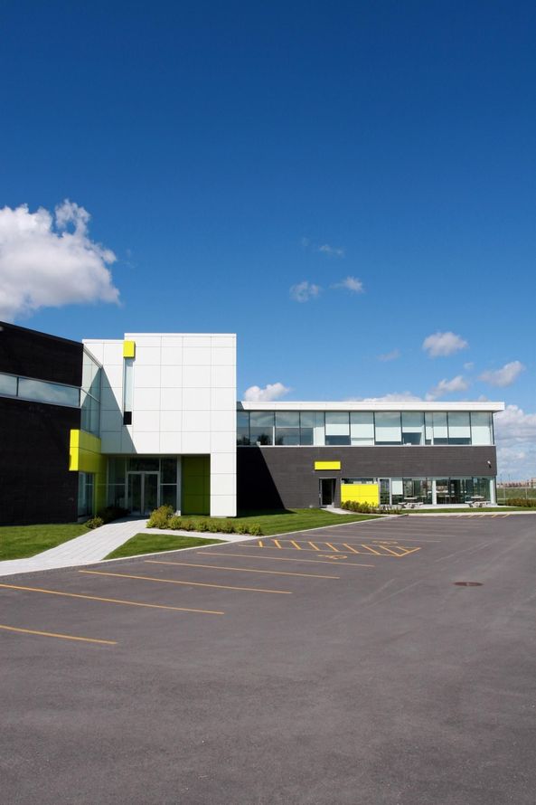 Modern building with white and dark gray facades beside a large empty parking lot under a blue sky
