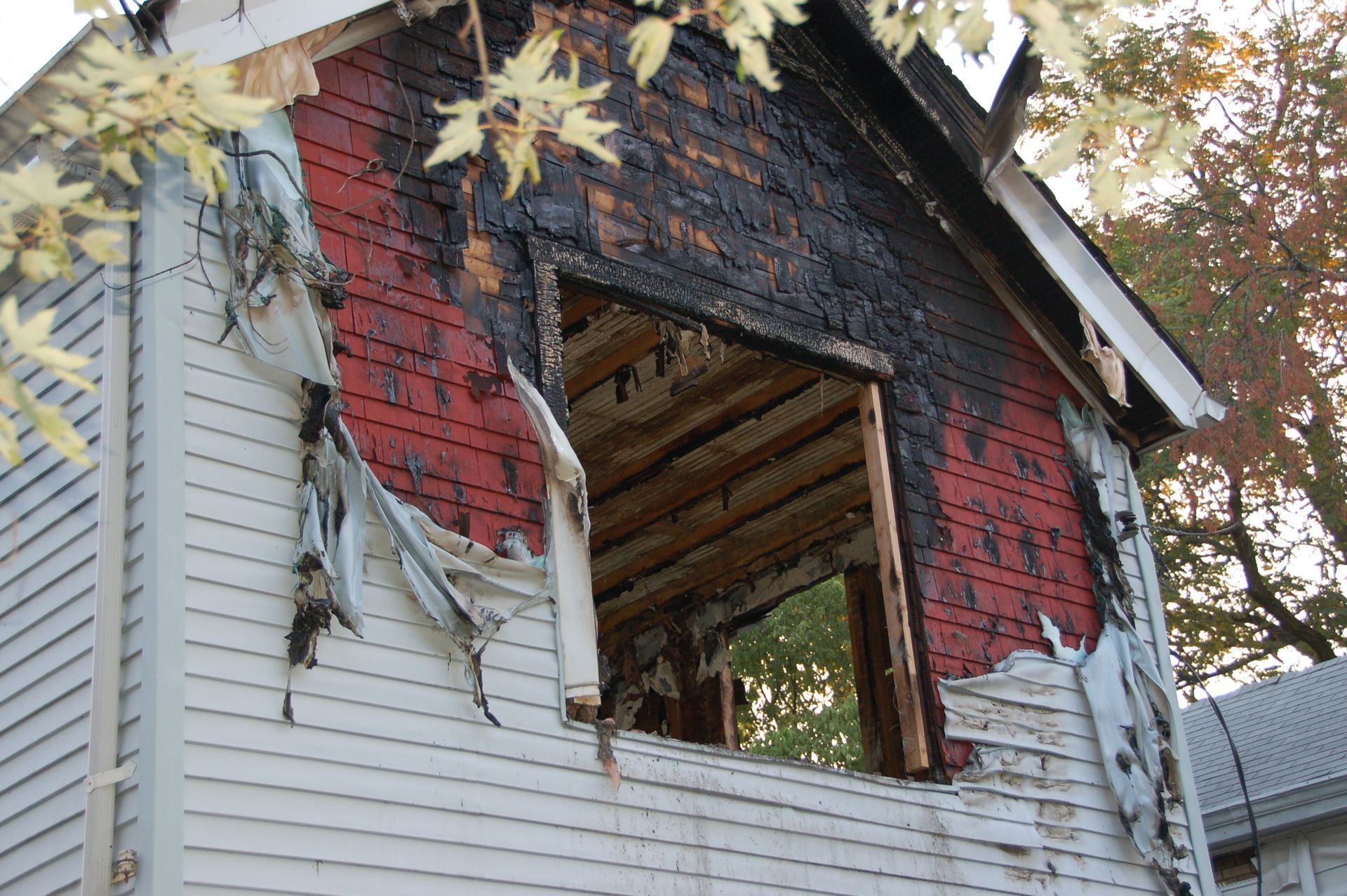 Exterior of a building damaged by fire, showing charred wood, a missing wall, and red siding.