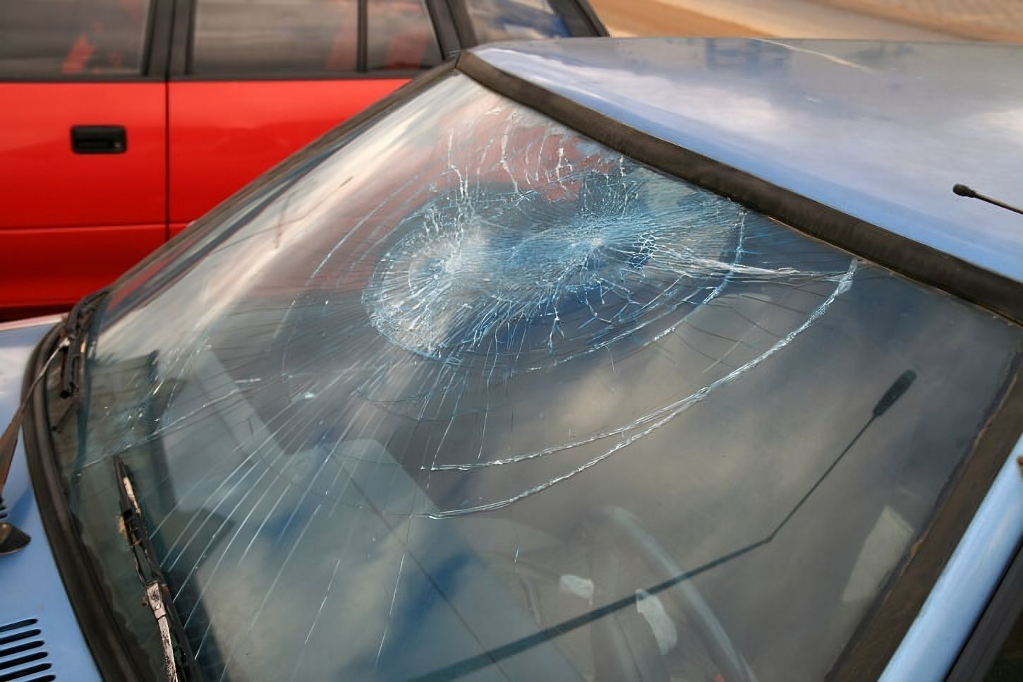 a blue car with a broken windshield is parked next to a red car .